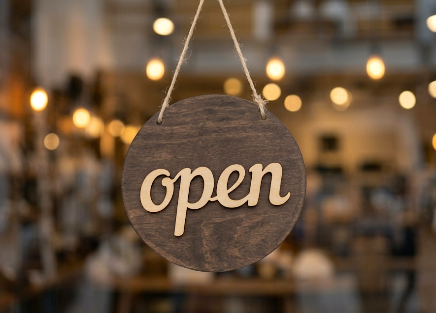 Wooden open sign hanging in the window of a warmly lit shop